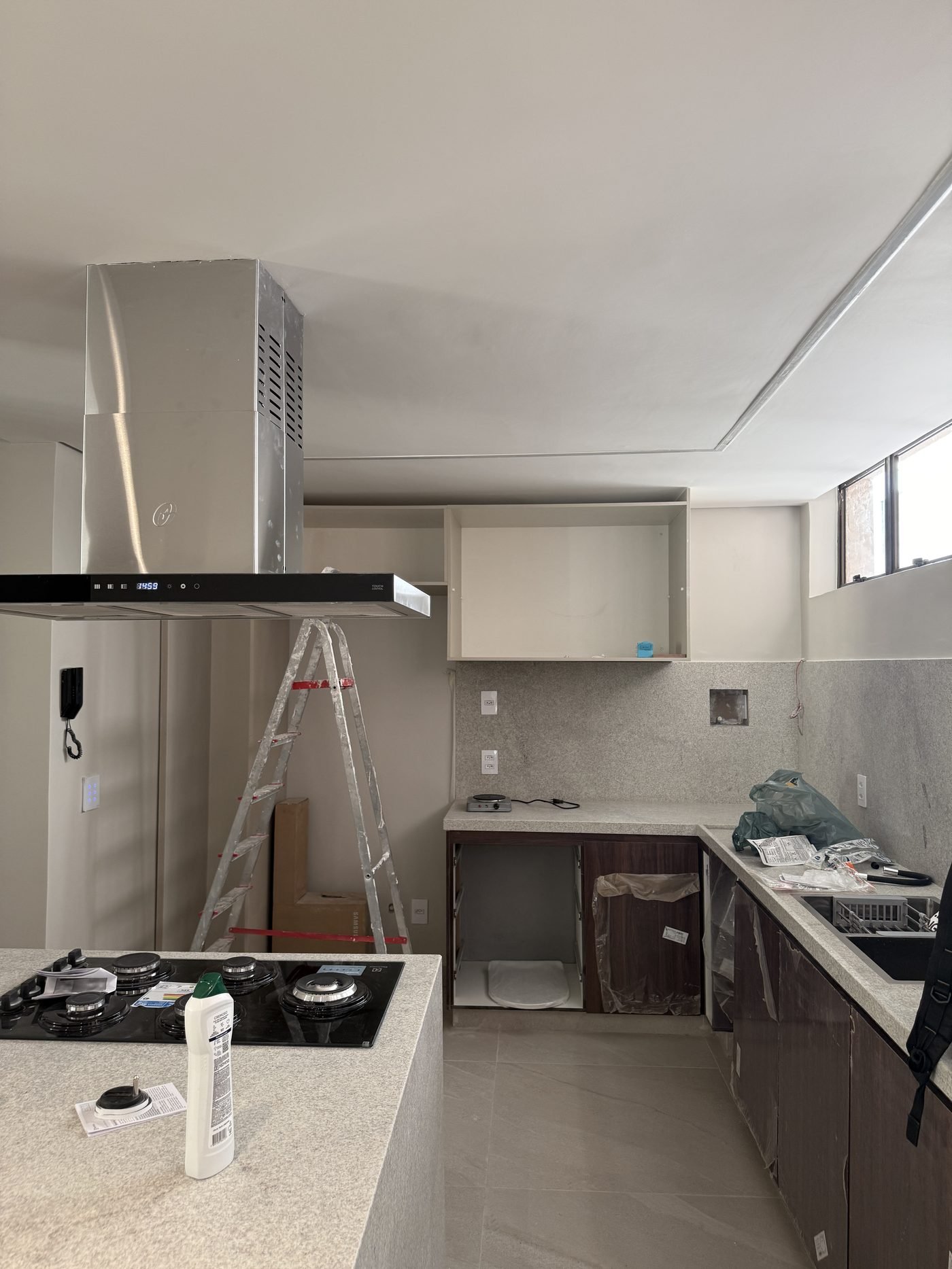 Cozinha de apartamento de alto padrão na região centro-sul de Belo Horizonte, com bancada e frontão em granito, cooktop, coifa de ilha e marcenaria em dois tons, obra da Apus Construtora