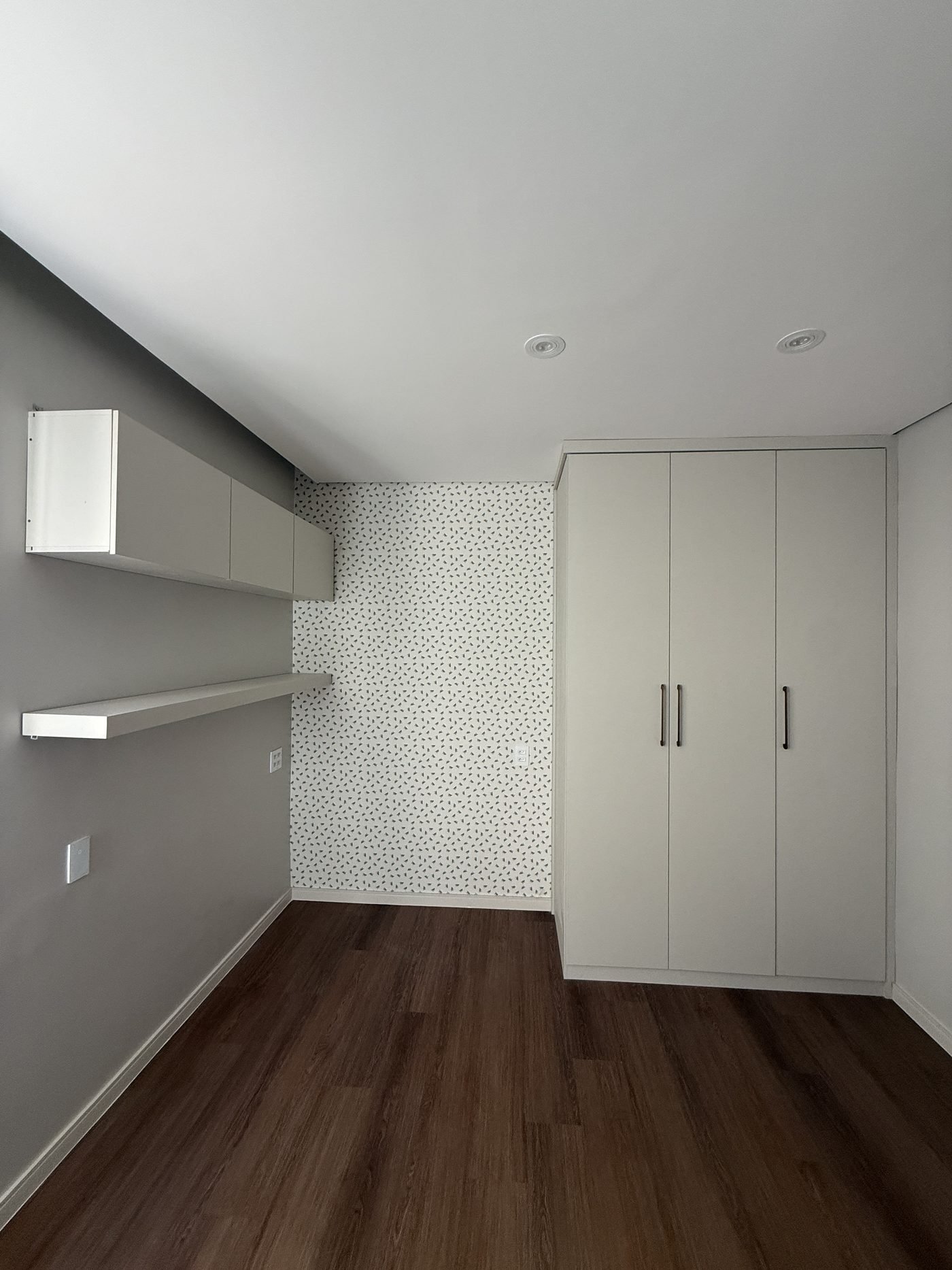 Quarto do apartamento com marcenaria planejada, prateleiras suspensas e papel de parede