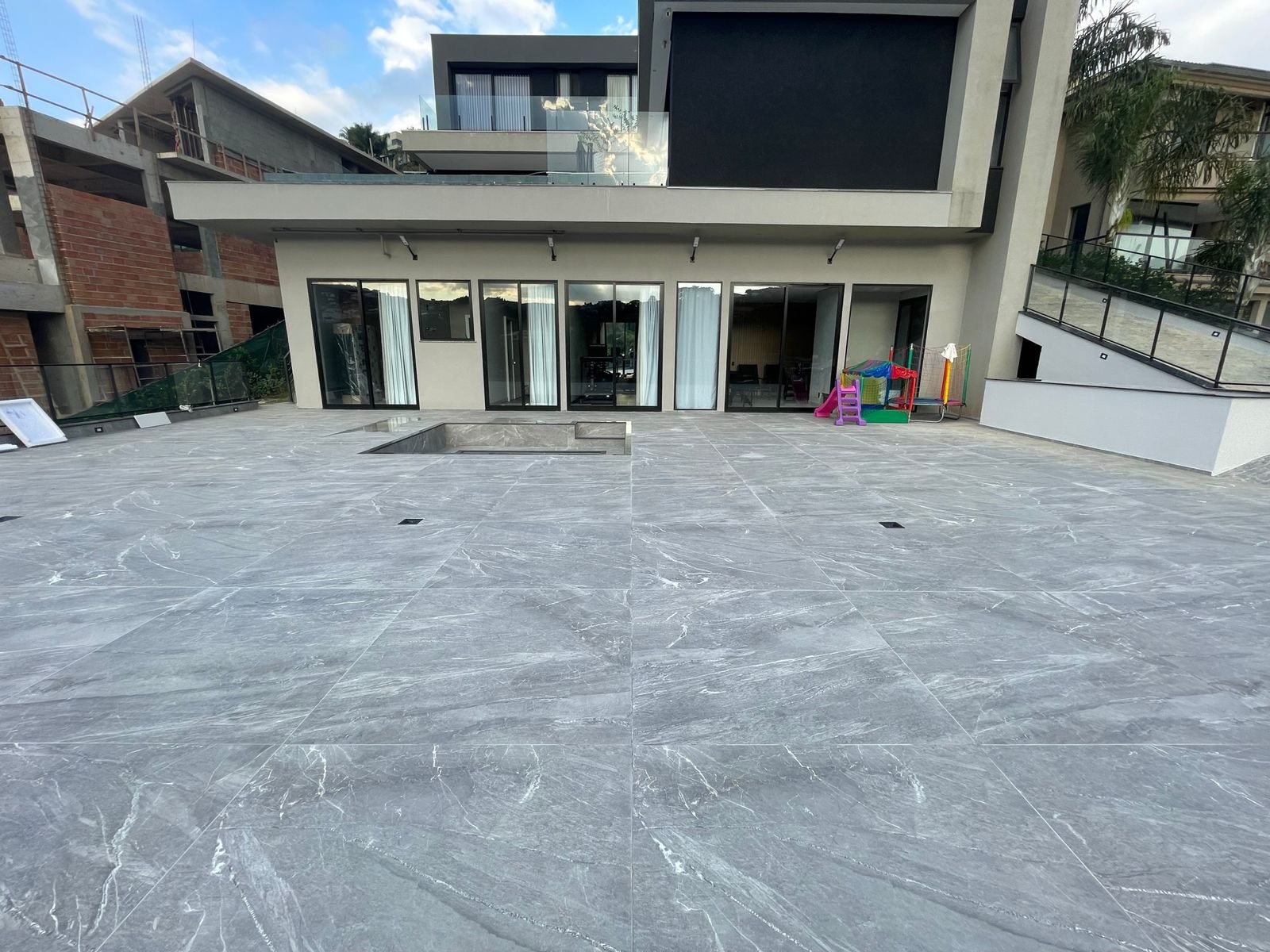 Área externa de casa em condomínio fechado de alto luxo executada pela Apus Construtora, com piso em porcelanato marmorizado de grande formato e piscina integrada ao deck