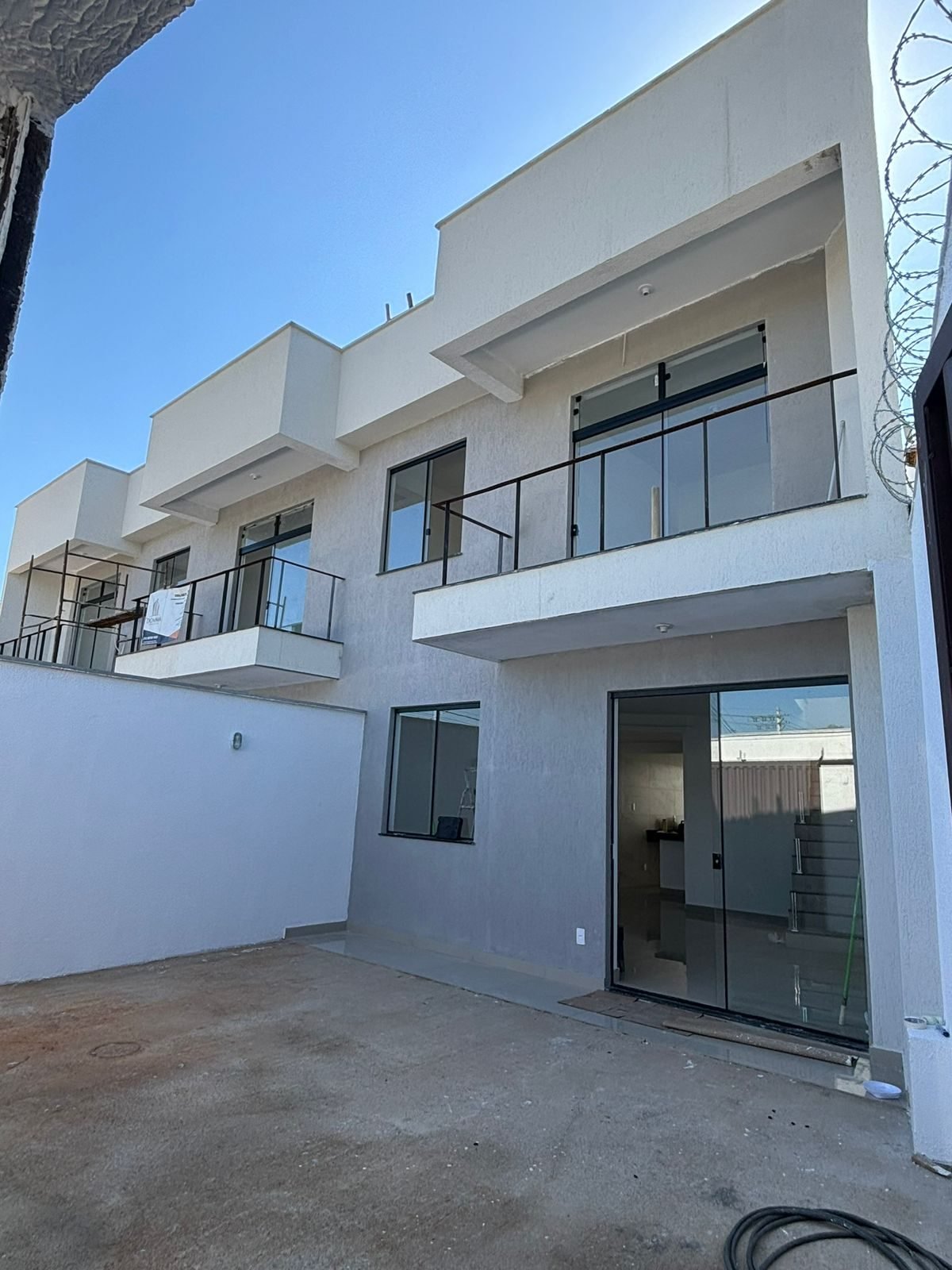 Fachada de três casas de 120 metros quadrados em Belo Horizonte, com sacadas em guarda-corpo de vidro e esquadrias em alumínio preto, obra da Apus Construtora