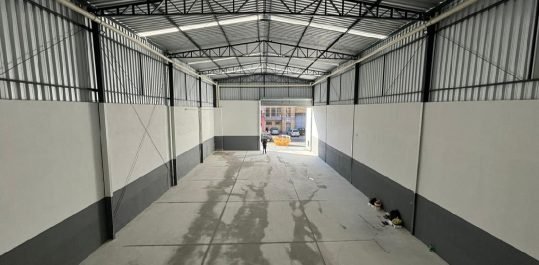 Vista interna do galpão em direção ao portão de acesso, com piso industrial em concreto